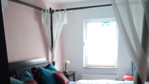 Ein Schlafzimmer mit einem Bett, Kissen, einem Nachttisch, einer Lampe und einem Fenster.
