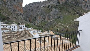 Un balcón con suelo de baldosas, con vistas a un pueblo de tejados de terracota y acantilados rocosos.