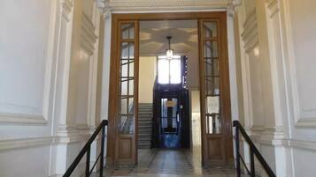 A grand staircase with ornate columns and a wooden railing, leading to a dark interior.