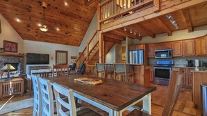 Eine geräumige Küche mit Holzausstattung, eine Essecke mit großem Tisch und Stühlen sowie eine Treppe, die in einen oberen Bereich führt.