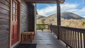 Eine hölzerne Veranda mit einer Bank, einer roter Tür und Blick auf eine hügelige Landschaft.