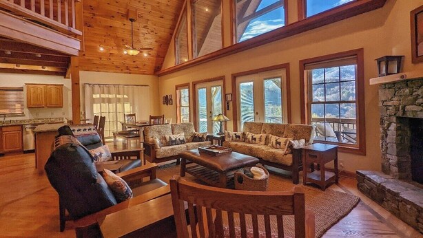 Ein geräumiges Wohnzimmer mit hohen Decken, großen Fenstern und einem Kamin aus Stein.