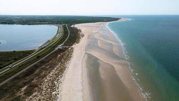 An aerial view of a coastal area with a curved road, a beach, and a large body of water. - Breathtaking Penthouse Views (Kamperland)