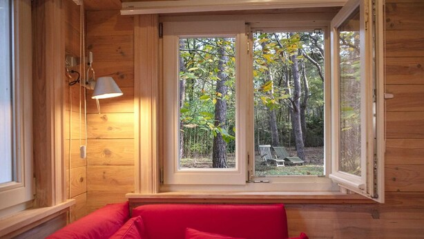 Ein Holzblockhaus-Interieur mit großem Fenster, einer roten Bank und einer Wandleuchte.