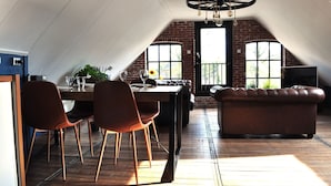 A dining area with a table, chairs, and a leather sofa in a loft-style room with exposed brick walls and large windows. - Shed 57b in an old flour mill in Haulerwijk (Haulerwijk)