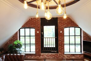 A room with exposed brick walls, a large window with a metal gate, and a ceiling with exposed beams and hanging light bulbs. - Shed 57b in an old flour mill in Haulerwijk (Haulerwijk)