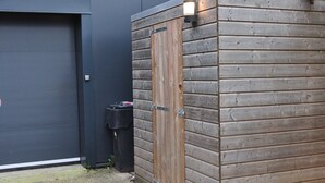 A building with a closed grey garage door, a wooden structure with a metal door, and a small black trash bin. - Shed 57b in an old flour mill in Haulerwijk (Haulerwijk)