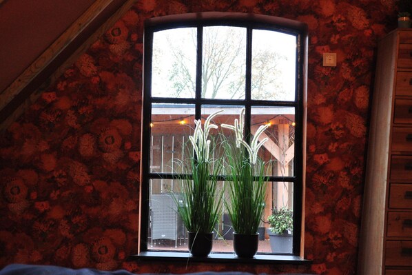 Una ventana con papel tapiz floral, techo de madera y vista a un edificio.
