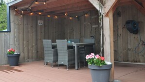 A covered patio with a wooden table and chairs, string lights, and potted plants. - Shed 57b in an old flour mill in Haulerwijk (Haulerwijk)
