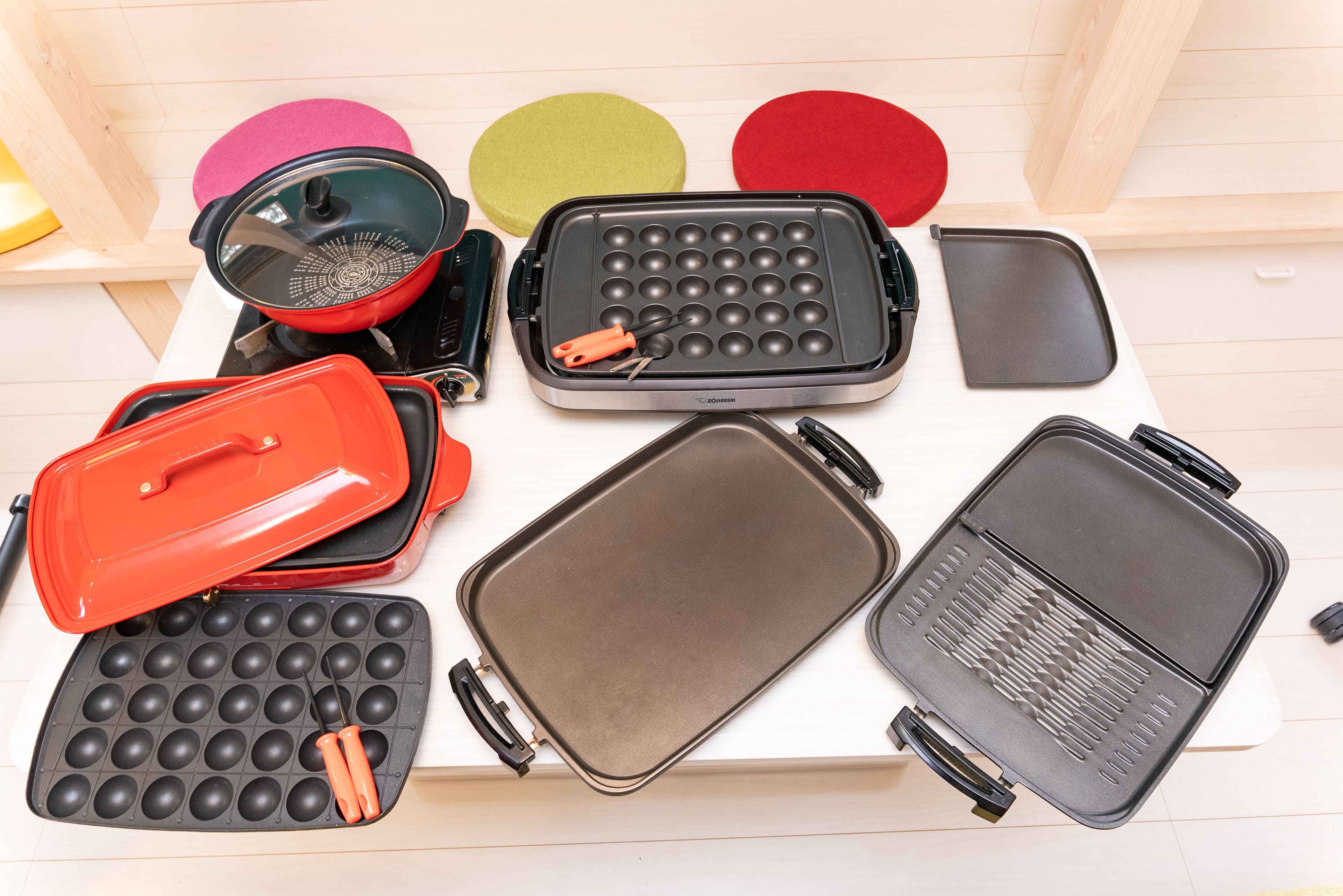 Variedad de electrodomésticos de cocina, incluyendo un fabricante de gofres, una sartén y una plancha, todo sobre una superficie de madera.