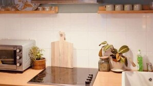 Una cucina con forno a incasso, piano cottura, tagliere di legno e ripiano con piatti e bicchieri.