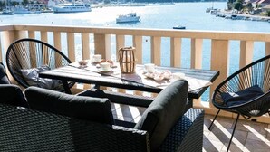 Un balcon agrémenté de meubles en osier, une table dressée avec des tasses et une théière, donnant sur une marina où sont amarrés des bateaux.