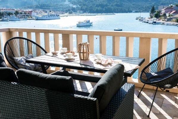 A balcony with wicker furniture, a table set with cups and a teapot, overlooking a marina with boats.