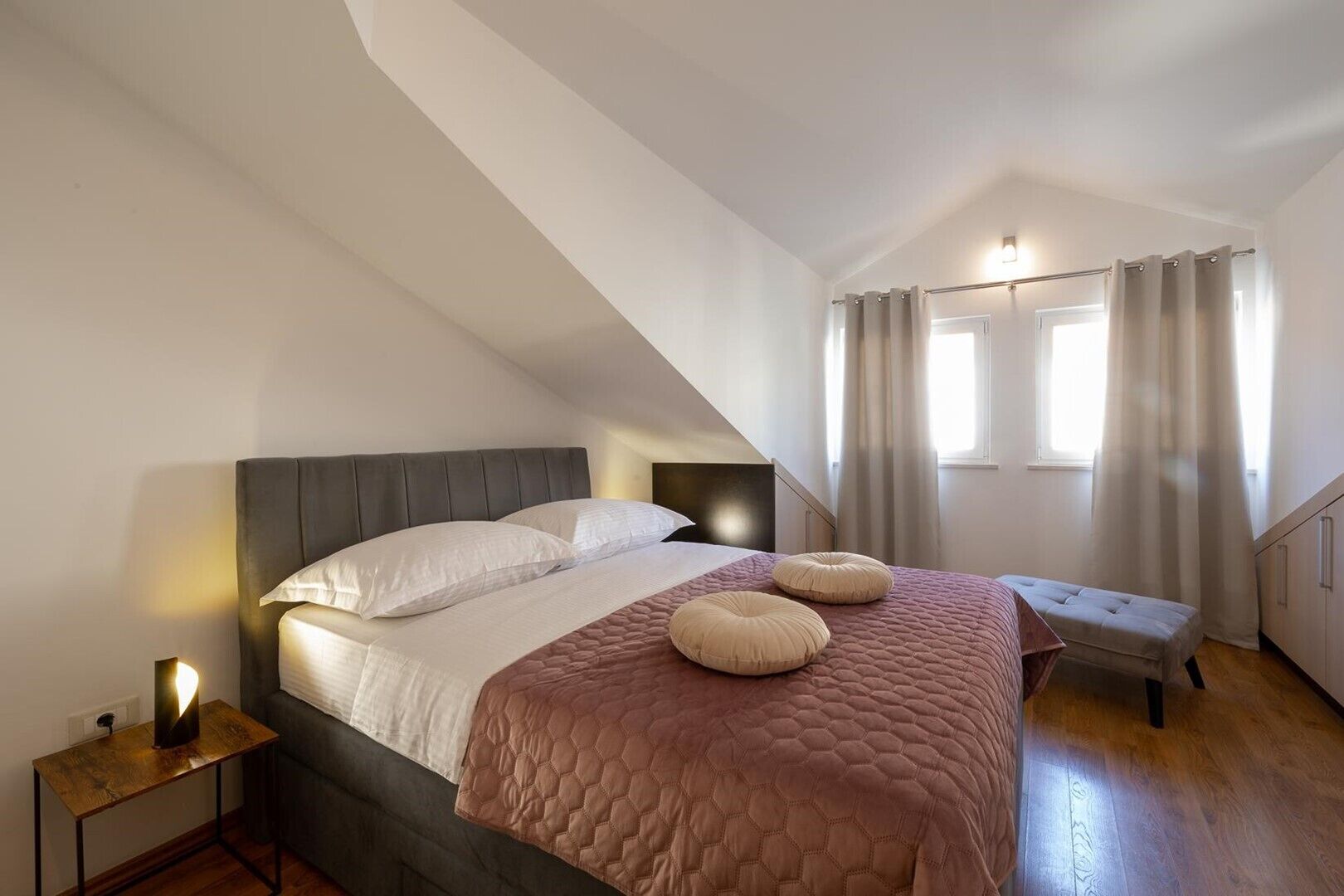A bedroom with a bed, bedside tables, a bench, and a window with curtains.