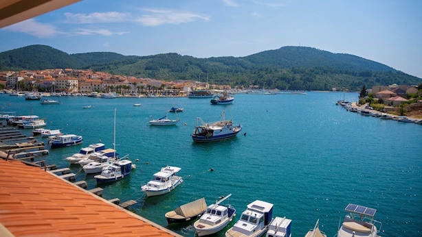 Un port de plaisance avec des bateaux amarrés, une ville côtière en arrière-plan et des montagnes.