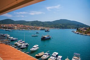 A marina with boats docked, a coastal town in the background, and mountains.