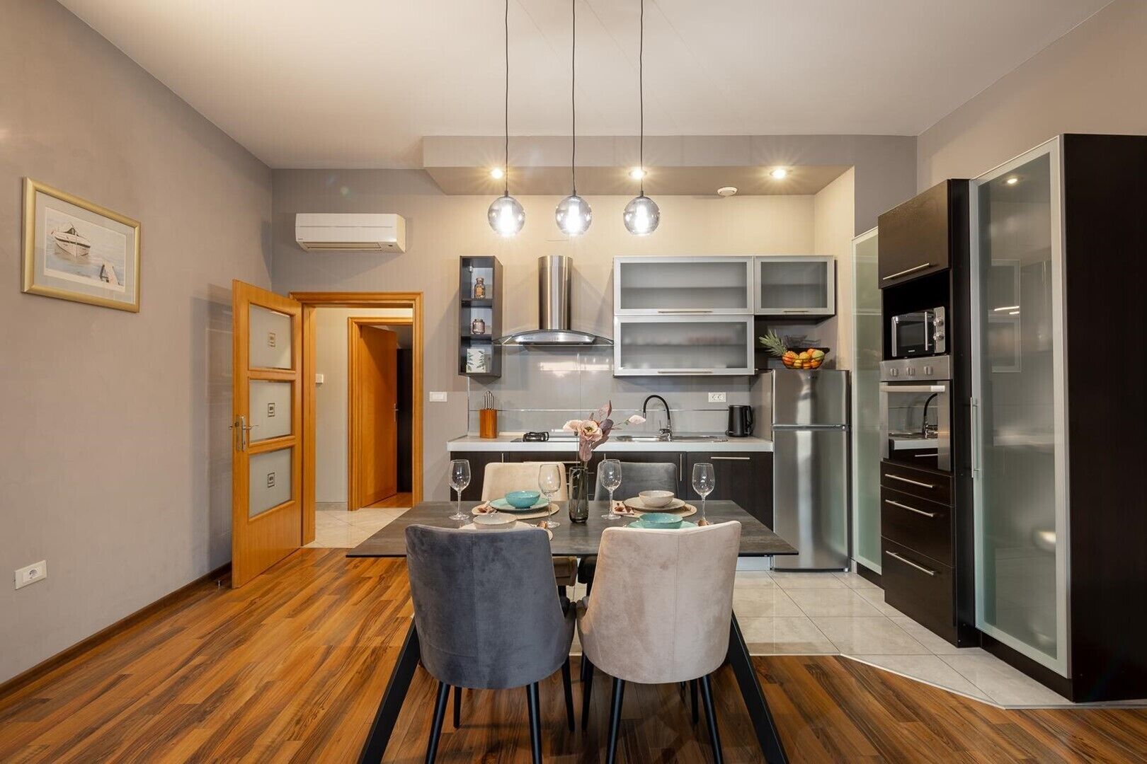 Une cuisine moderne avec un coin repas, dotée d’un plancher en bois, d’une table à manger avec des chaises, d’un réfrigérateur et d’un four à micro-ondes.