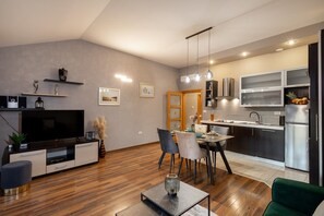 Een moderne woonkamer met een flatscreen televisie, een eethoek met een tafel en stoelen, en een keuken met roestvrijstalen apparatuur.