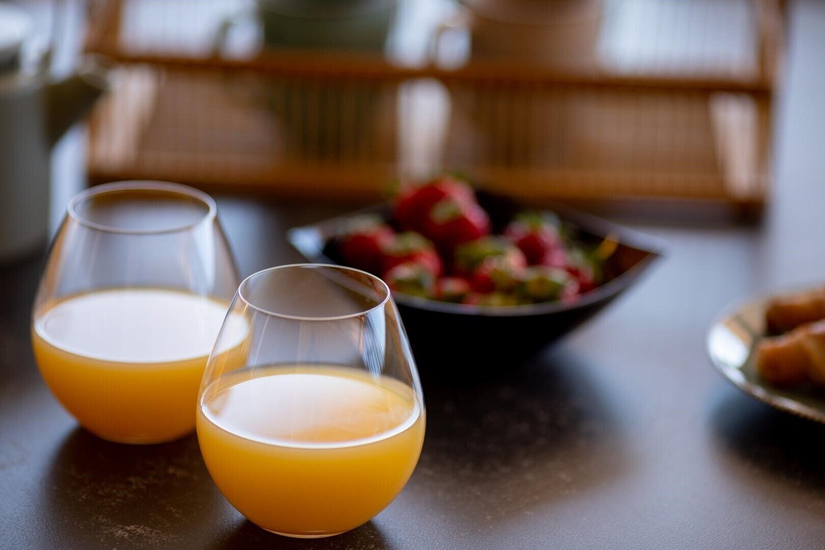 Zwei Gläser Orangensaft auf einem Tisch, im Hintergrund eine Fruchtschale.