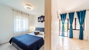 Een slaapkamer met een bed, gordijnen, een nachtkastje en een wandlamp.