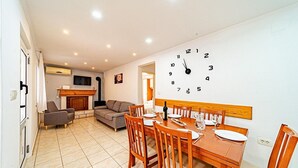 Een woonkamer met een bank, een televisie en een open haard. Er is een eethoek met een houten tafel en stoelen.