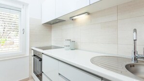 Eine moderne Küche mit weißen Schränken, einer Spüle aus Edelstahl und einem Fenster mit Jalousien.