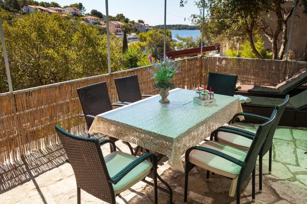An outdoor patio with a table and chairs, surrounded by a bamboo fence, overlooking a scenic view of houses and a body of water.