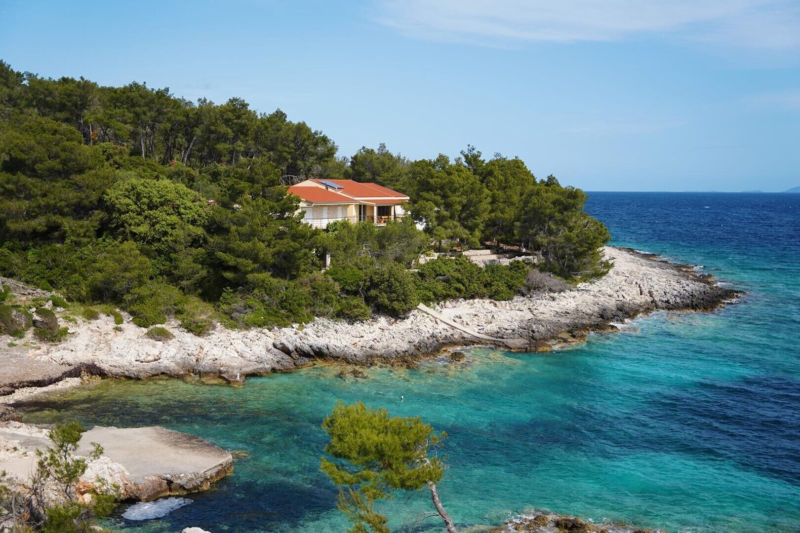 A coastal house surrounded by trees and rocky shoreline.