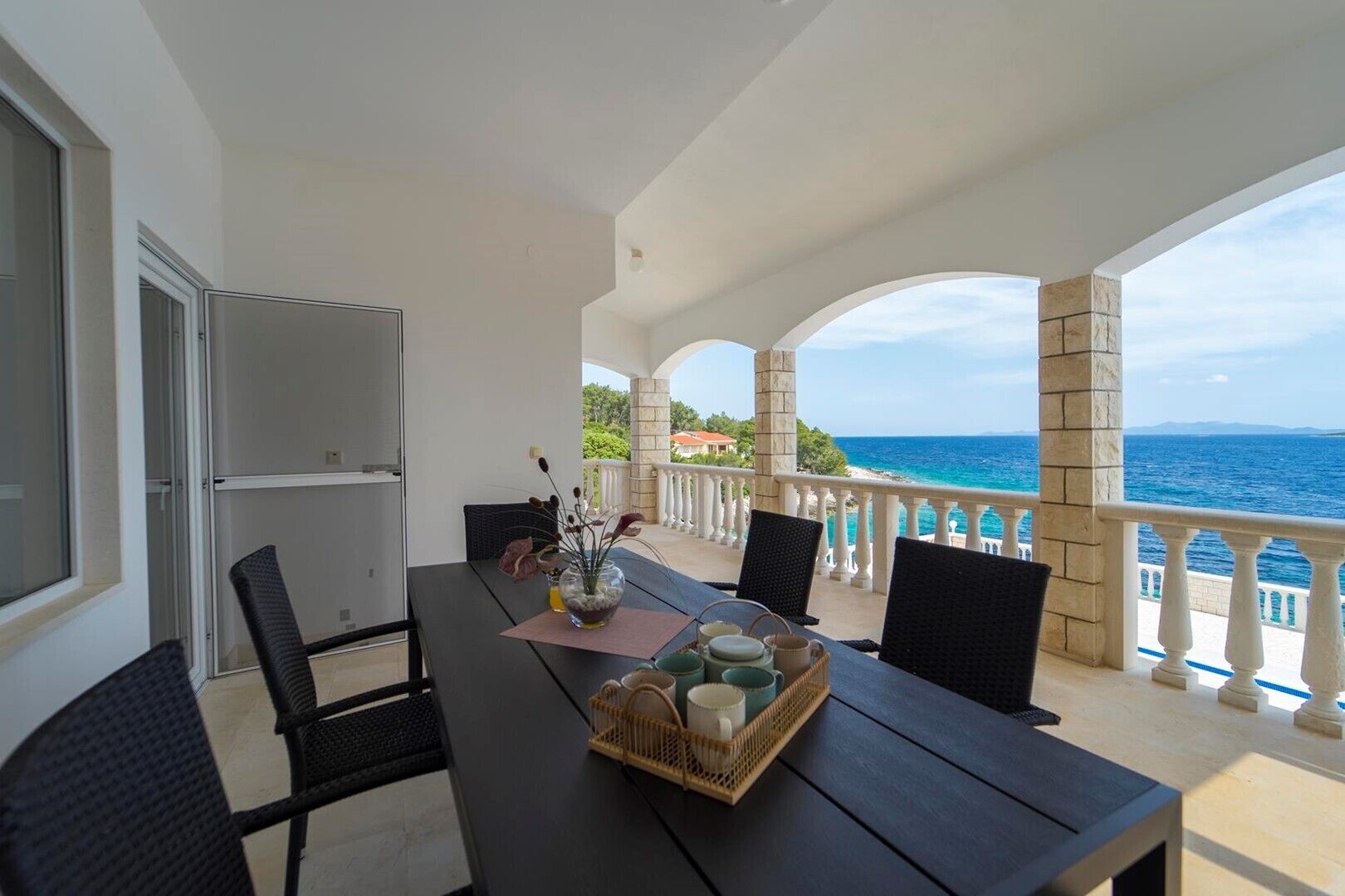 Een balkon met een tafel en stoelen, met uitzicht op de zee.