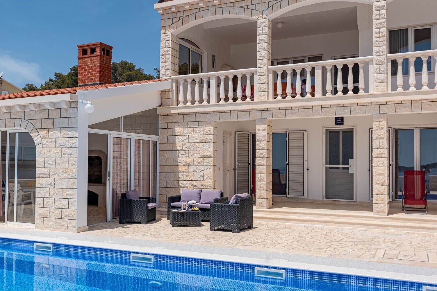 A two-story building with a pool, stone facade, and outdoor seating area.