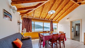 A cozy room with a wooden ceiling, a dining table with chairs, a sofa with cushions, and a view of the sea through large windows. - Beautiful Villa with private pool and sea view (Vela Luka)