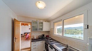 A compact kitchen with a view of a lake, a dining area with a table and chairs, and a door leading to another room. - Beautiful Villa with private pool and sea view (Vela Luka)