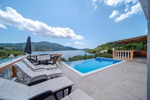 Zona junto a la piscina con sillones de descanso y vistas a un lago y montañas.