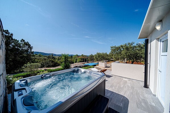 A hot tub with a view of a pool and mountains, surrounded by greenery.