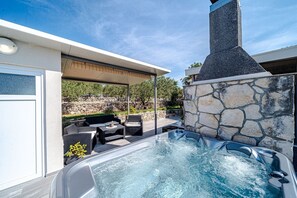 Ein Whirlpool mit Steinwand und Kamin, Sitzgelegenheiten im Freien und ein klarer Himmel.