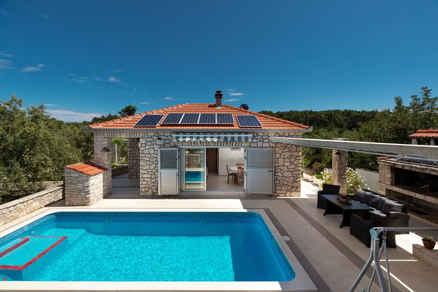 Ein Steinhaus mit Swimmingpool, Solaranlage und Gartenmöbeln.