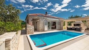 Une maison en pierre avec une piscine, un espace salon extérieur et une cheminée.