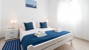 Une chambre d’hôtel avec un lit, deux tables de chevet, une commode, une fenêtre avec des rideaux et un tableau au mur.