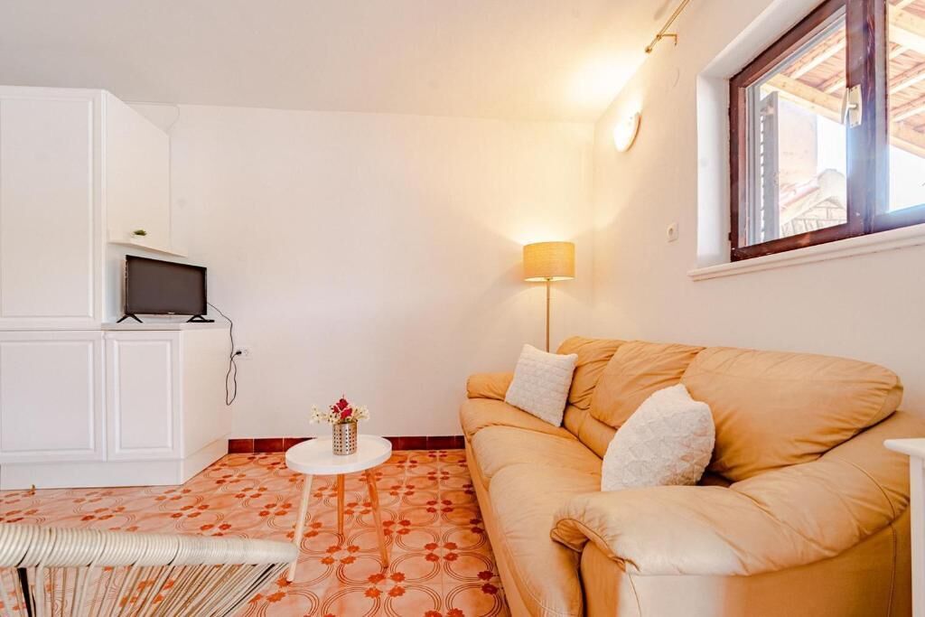 Un salon chaleureux avec un canapé, une petite table ronde sur laquelle est posé un vase, un téléviseur sur un meuble et une lampe.