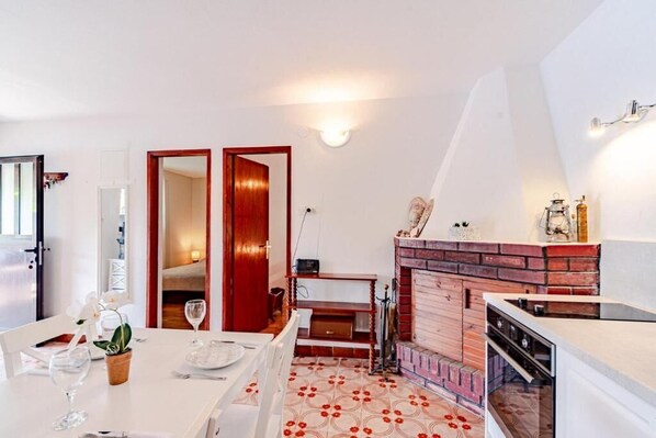 Una cocina compacta con chimenea de ladrillo, paredes blancas y una zona de comedor con una mesa dispuesta para dos.