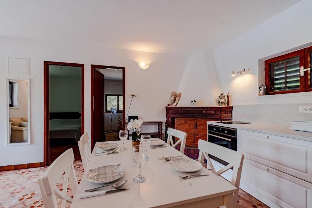 Zona pranzo con tavolo apparecchiato per quattro, cucina con piano cottura e forno, e un armadietto in legno con oggetti decorativi.