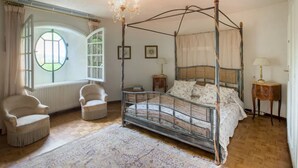 Un letto a baldacchino con tenda, una finestra rotonda, due poltrone, un piccolo comodino e una lampada da terra.