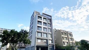 Un edificio a più piani con un design architettonico moderno, caratterizzato da un rivestimento in vetro e cemento e diversi balconi.