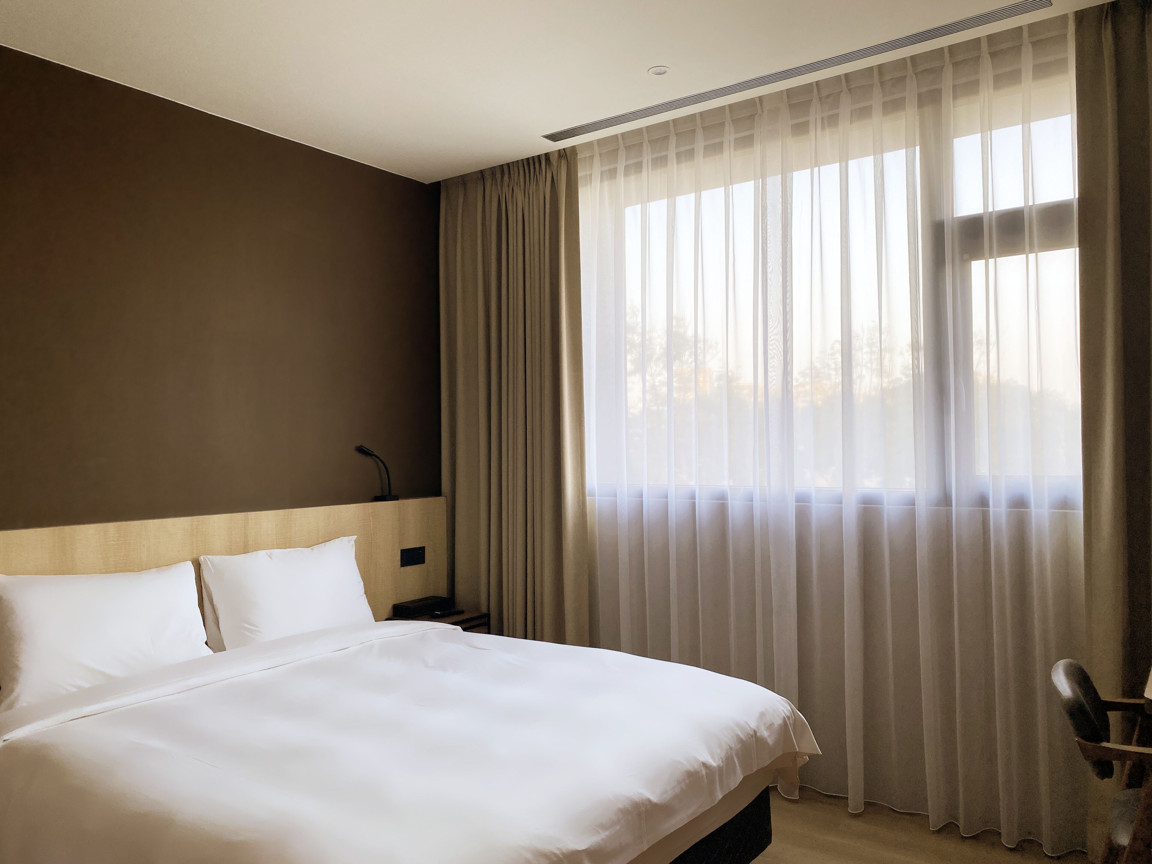 A hotel room with a large bed, a headboard, a bedside table, and a chair.