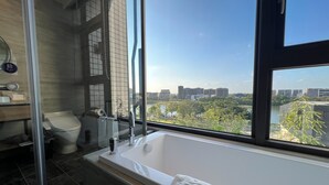 Uma casa de banho moderna com banheira, sanita e lavatório, com uma grande janela e vista para a cidade.