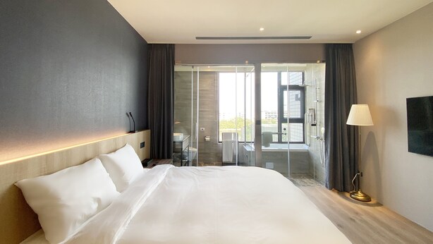 Quarto de hotel moderno com cama grande, chuveiro com box de vidro e vista para o exterior.