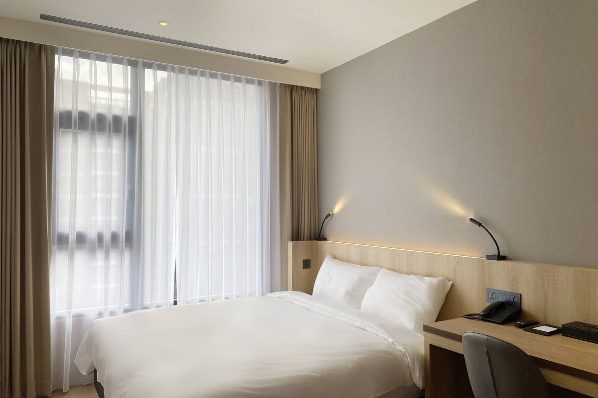 Une chambre d’hôtel avec un grand lit, un bureau avec une chaise, un téléphone et une lampe fixée au mur.