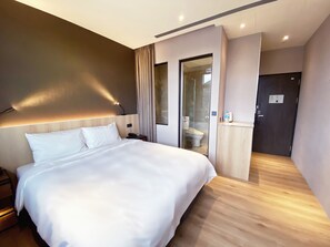 A modern hotel room with a large bed, a bedside table, a nightstand, a bathroom with a shower, and a toilet visible through a glass door. - alfar Hotel (Taoyuan City)
