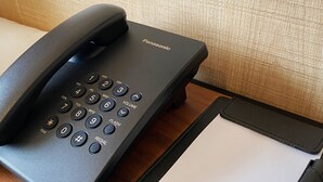 Um telefone sem fio Panasonic, uma carteira de couro preta e uma caneta sobre uma superfície de madeira.