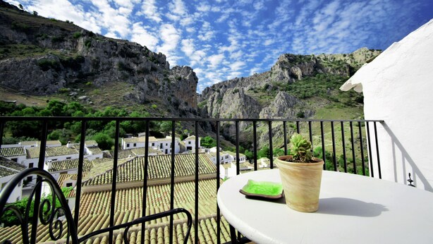 A balcony with a potted plant, a table, and a view of a village with terracotta roofs. - El Orgullo rural house, with terrace and impressive views of the Bailón Canyon. (Zuheros)